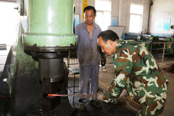 李根生和工友配合在空氣錘前趕工自制件